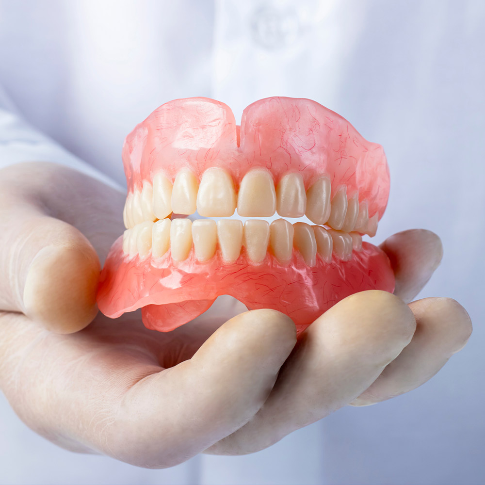 Dentist holding complete dentures model showing full upper and lower teeth prosthetics