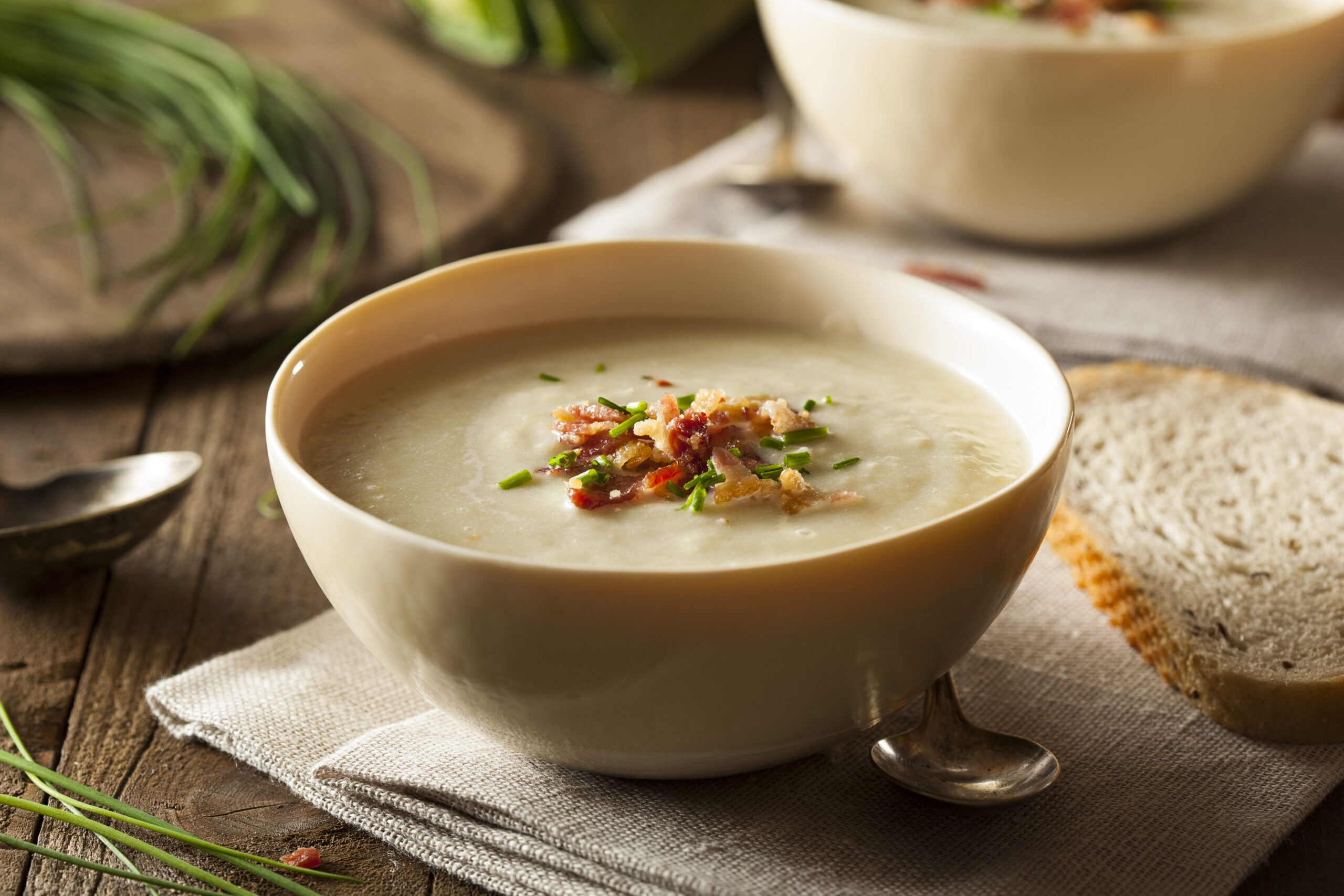 Creamy soup in ceramic bowl garnished with herbs and crispy bacon bits, served with bread.
