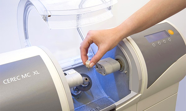 Dentist's hand operating CEREC milling machine for digital dental restoration fabrication.