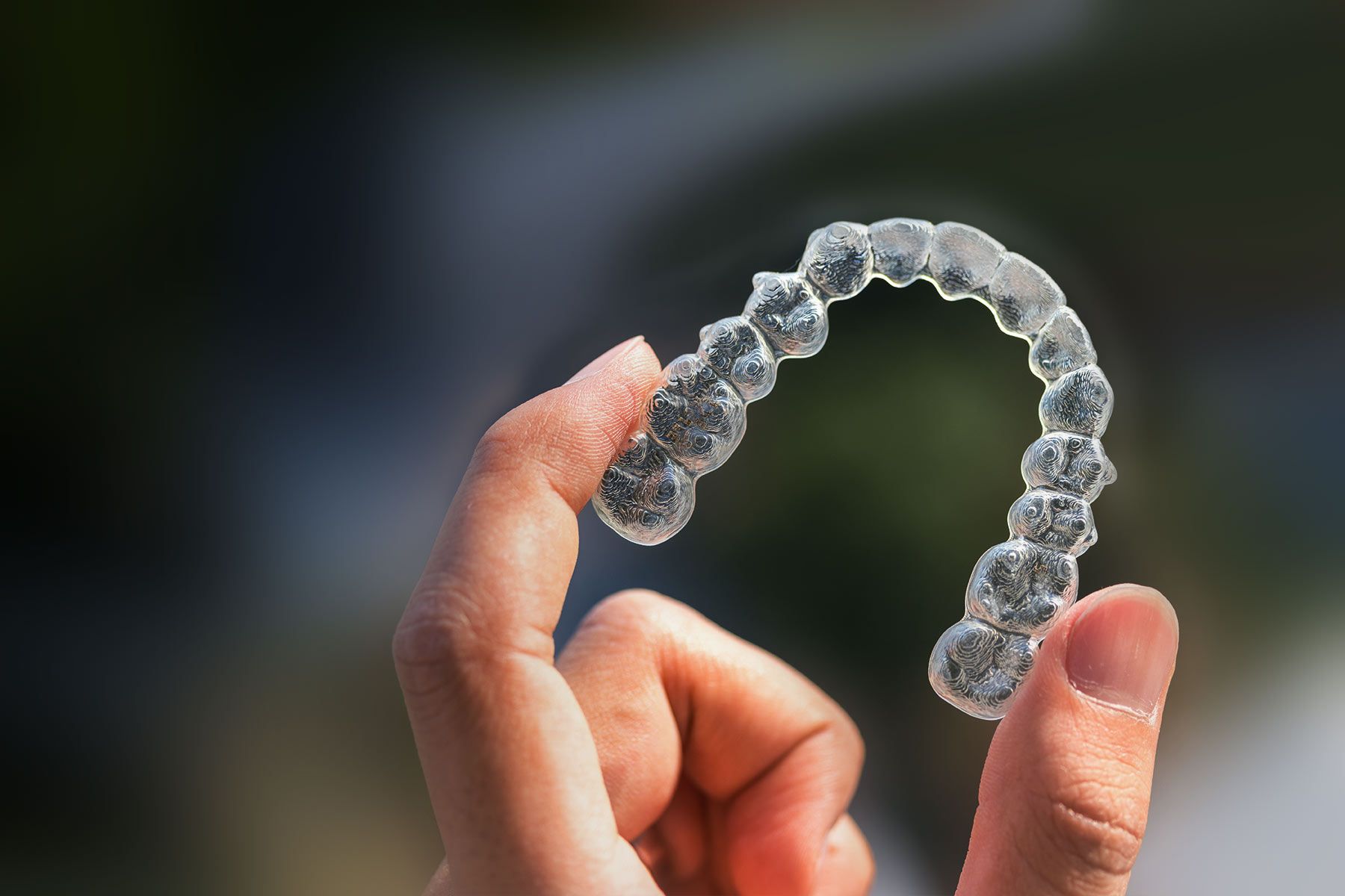 Hand holding clear plastic dental aligner against blurred natural background