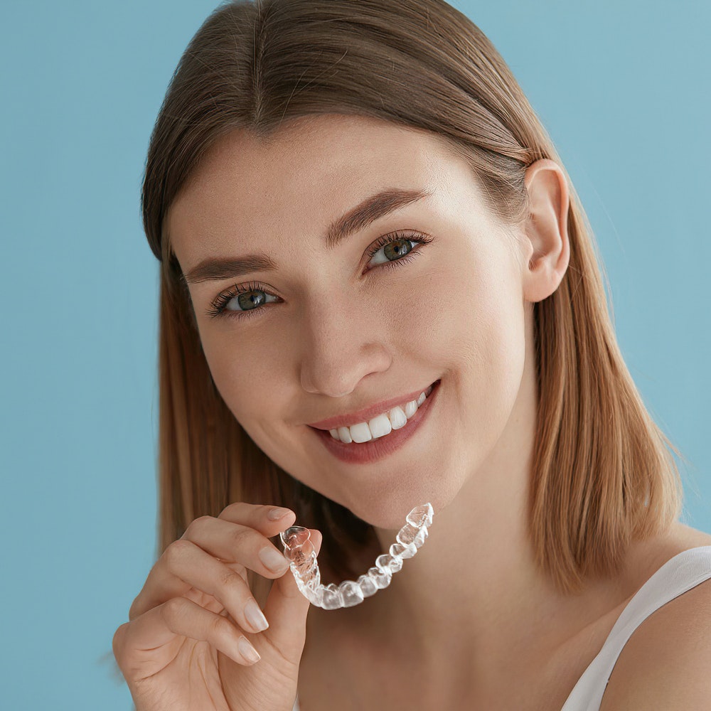 Young woman smiling while holding clear dental aligner against blue background.
