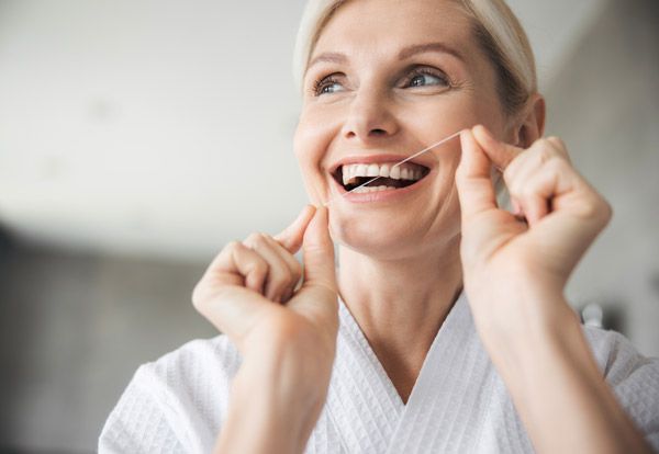 Smiling woman applying skincare product to face in bright, modern bathroom setting.