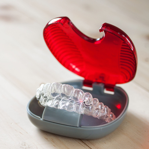 Clear plastic retainer in red case on white surface, dental care product