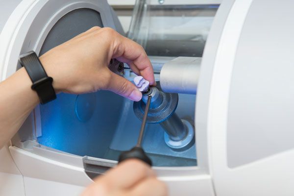 Hand inserting blue dental aligner into clear tray during orthodontic treatment application.