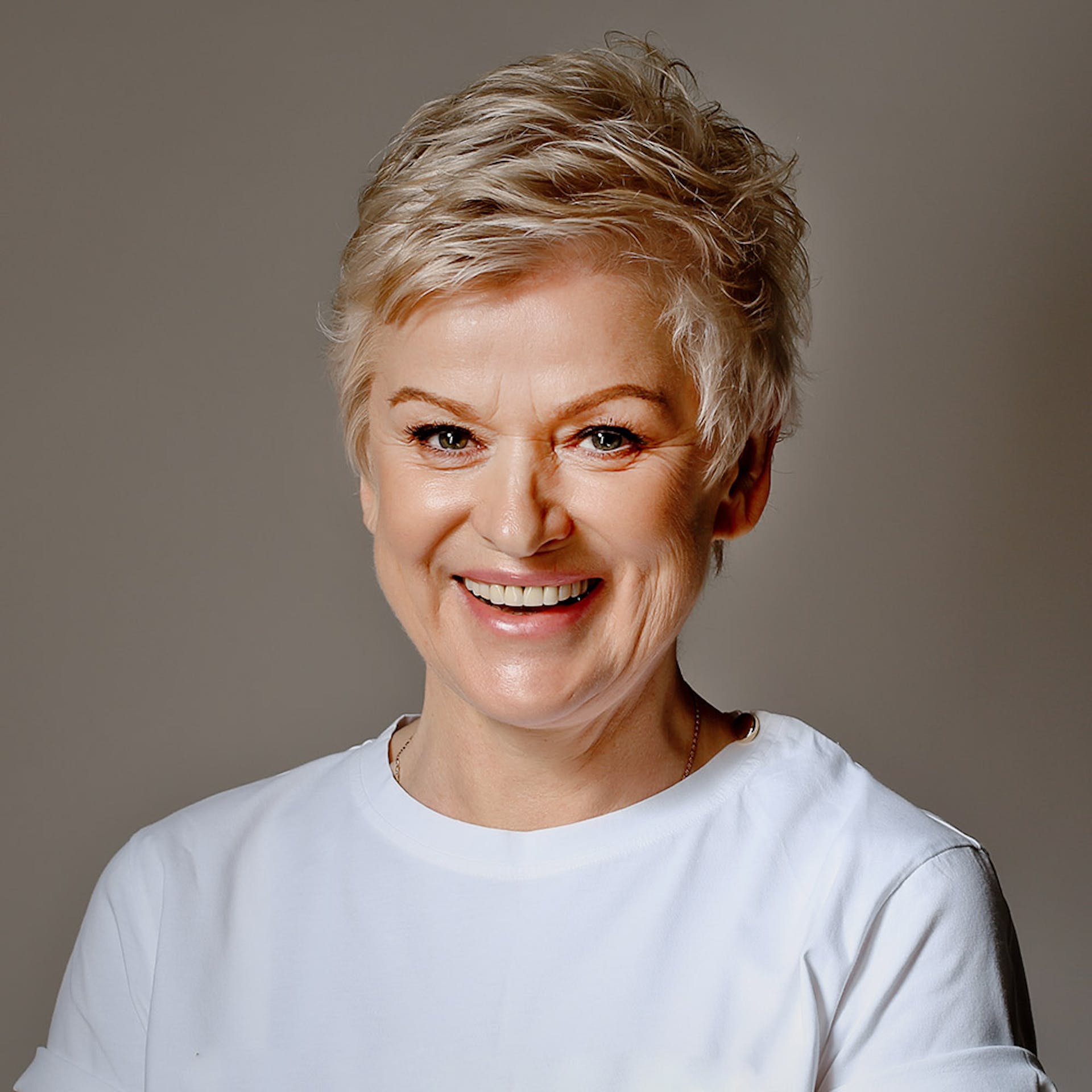 Woman with short blonde hair smiling at camera in professional portrait wearing light blue shirt