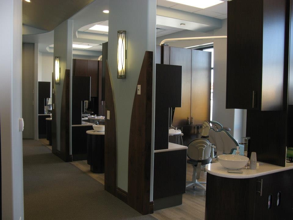 Modern dental office bathroom with multiple sinks, mirrors, and dark cabinetry fixtures.