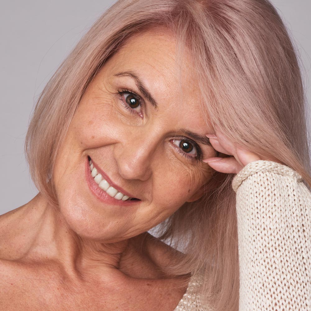 Smiling mature woman with pink hair in professional headshot against neutral background.